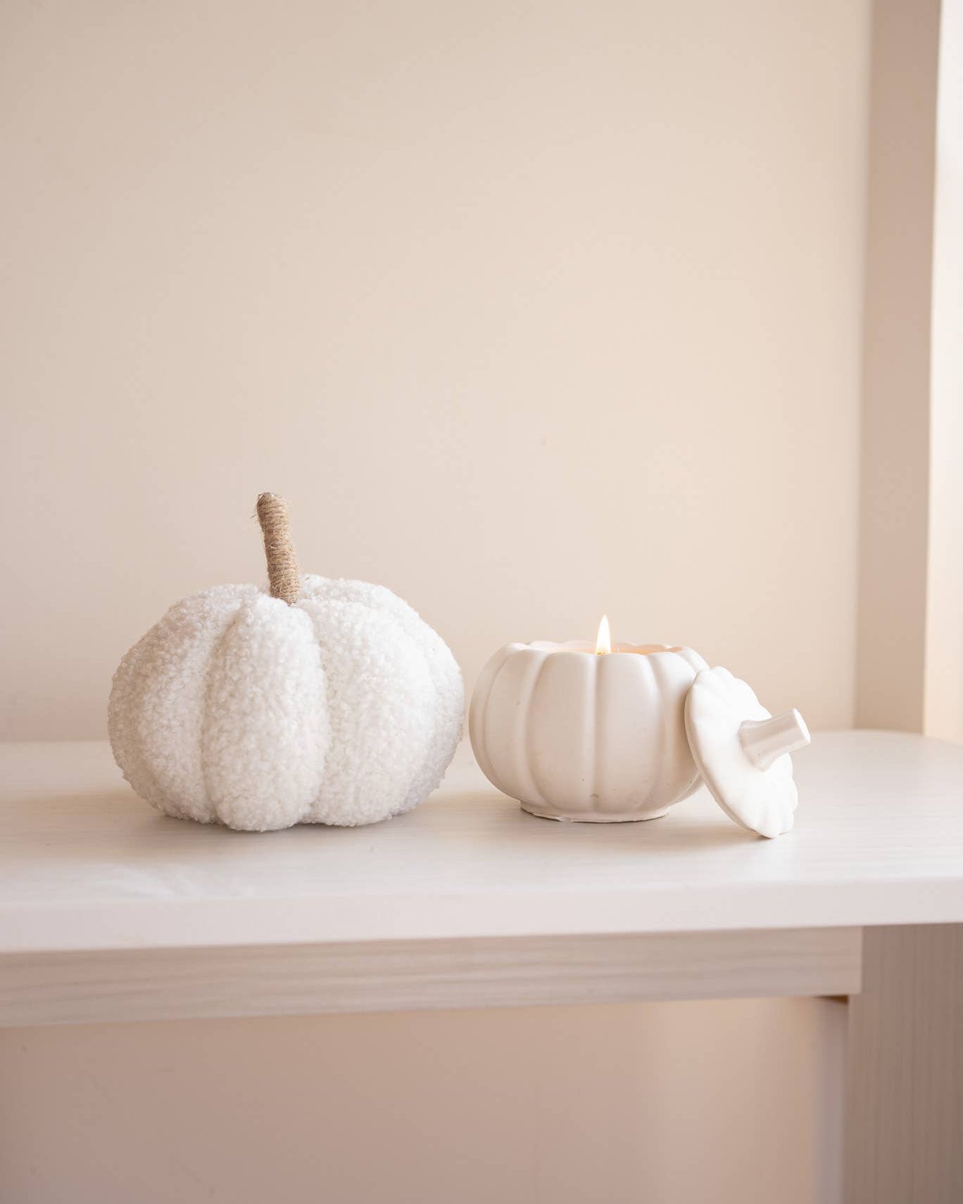 White textured pumpkin and candle on a white surface with a neutral background