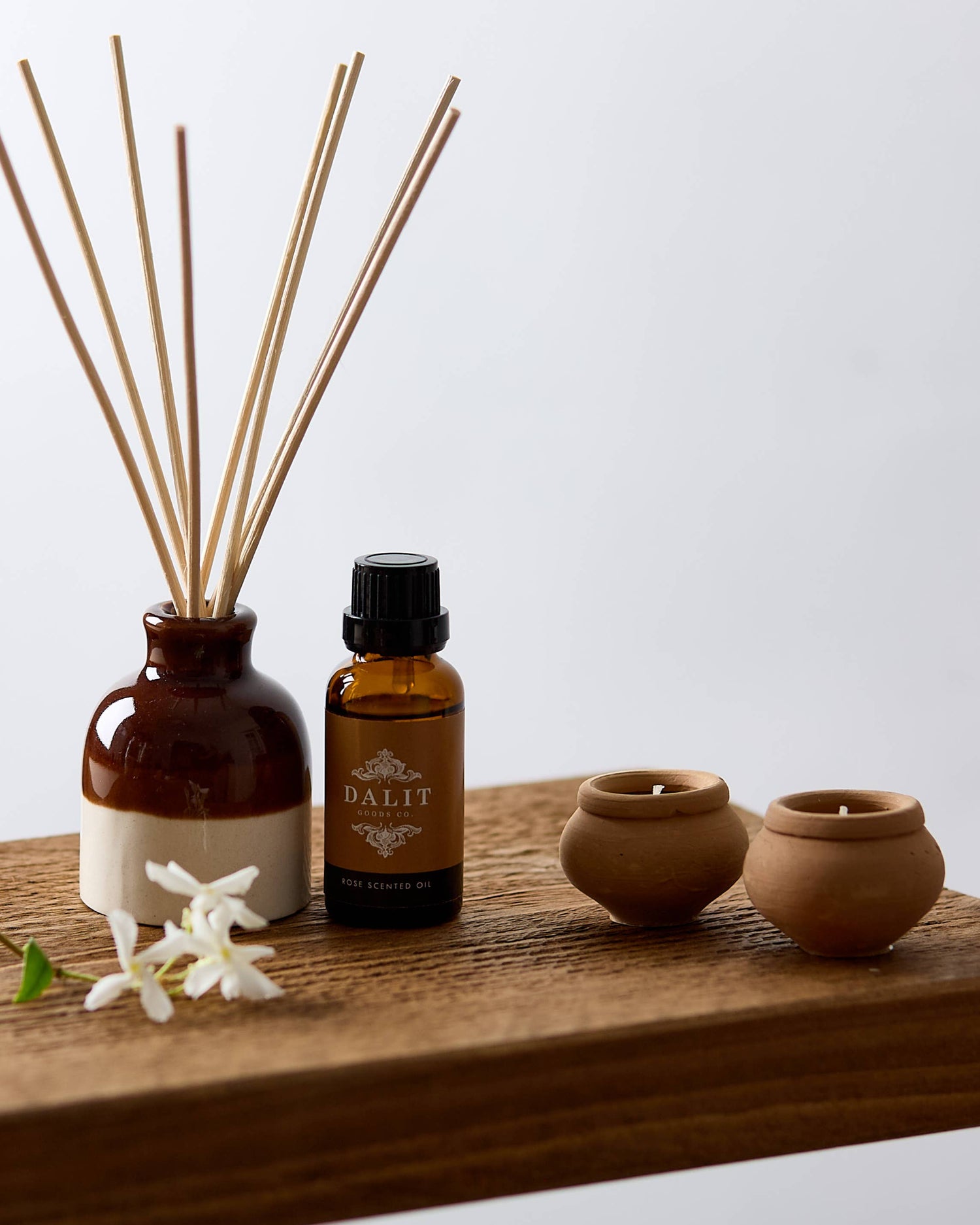Set of essential oils, diffuser, and small containers on a wooden board with a white background