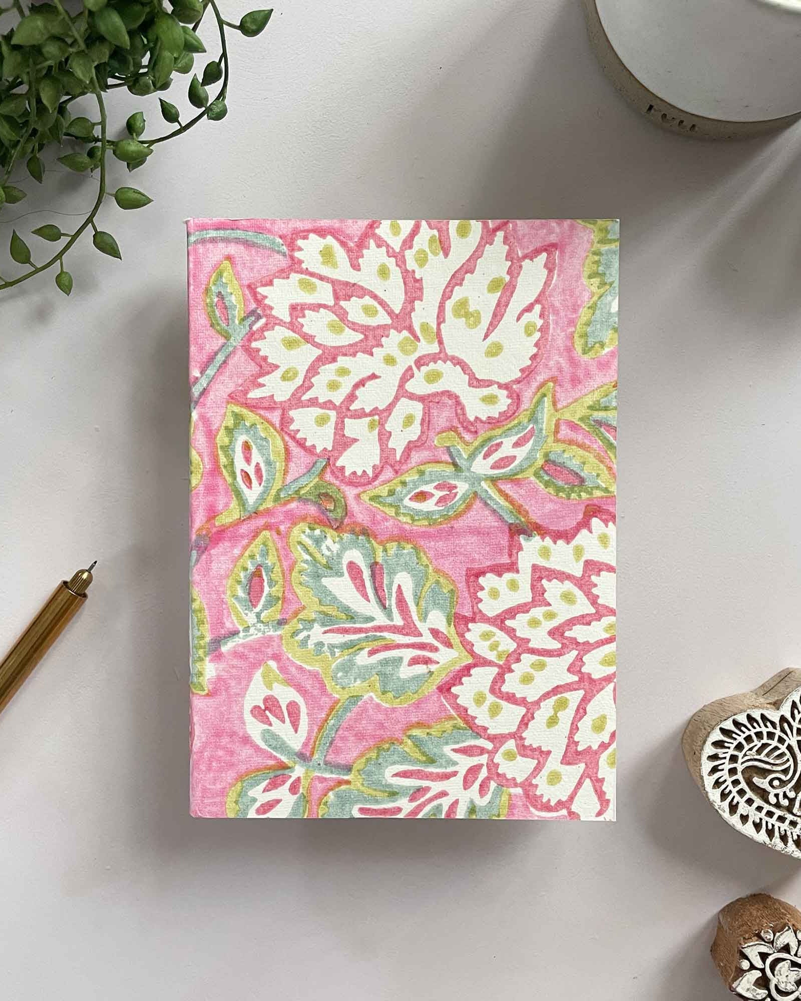 Notebook with pink floral pattern on a white surface with decorative items.