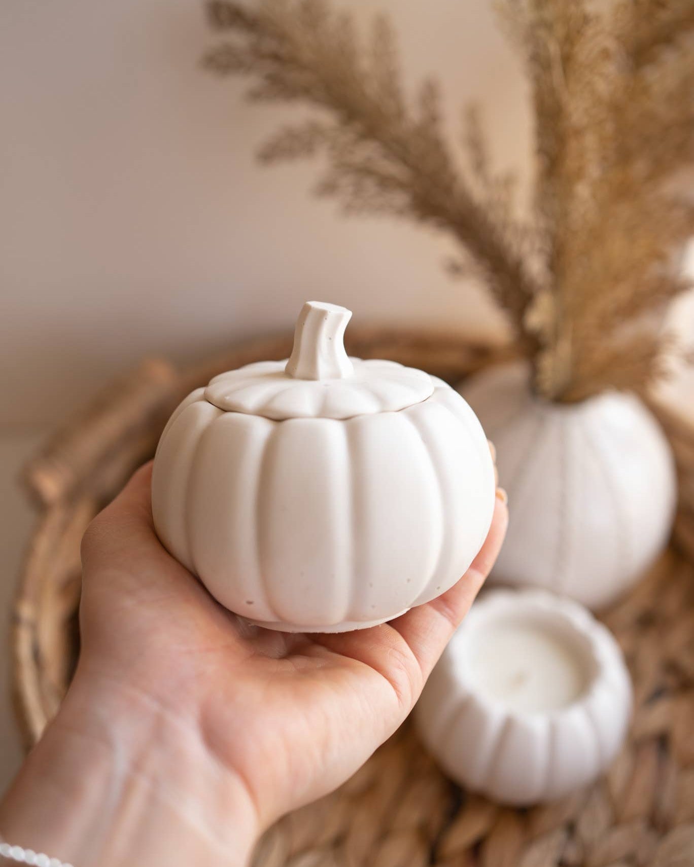 Hand holding a small white pumpkin with decorative elements in the background
