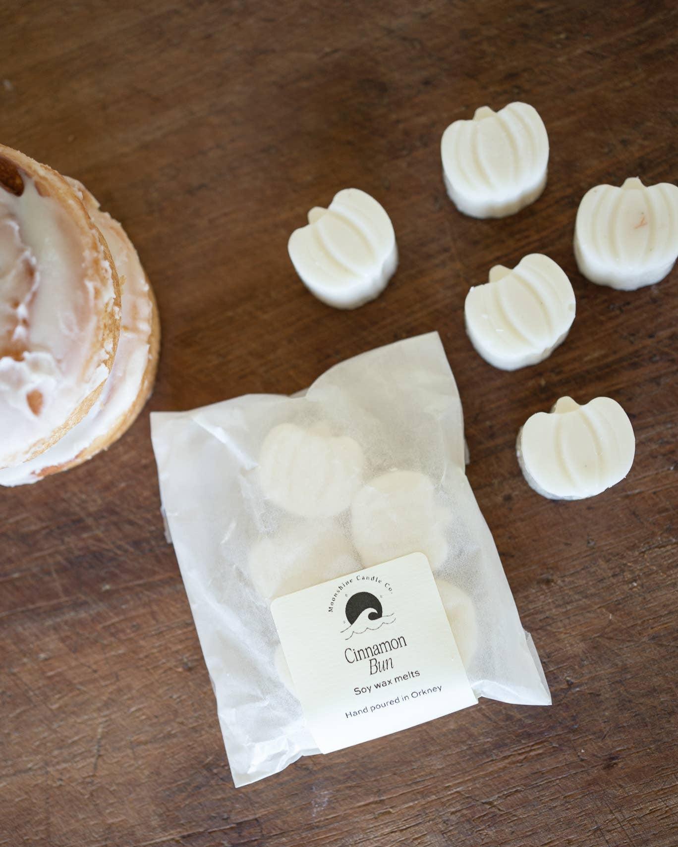 White wax melts in pumpkin shapes on a wooden surface with a branded paper bag.