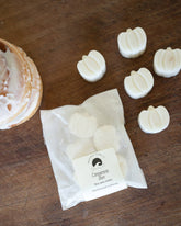 White wax melts in pumpkin shapes on a wooden surface with a branded paper bag.