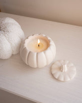 White ceramic pumpkin with a lit candle inside on a white surface