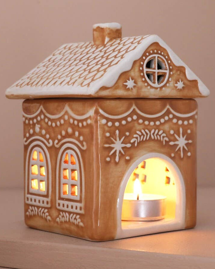Decorative gingerbread house-shaped lantern with a lit candle inside on a beige background