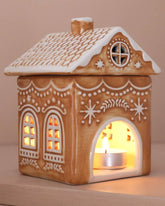 Decorative gingerbread house-shaped lantern with a lit candle inside on a beige background