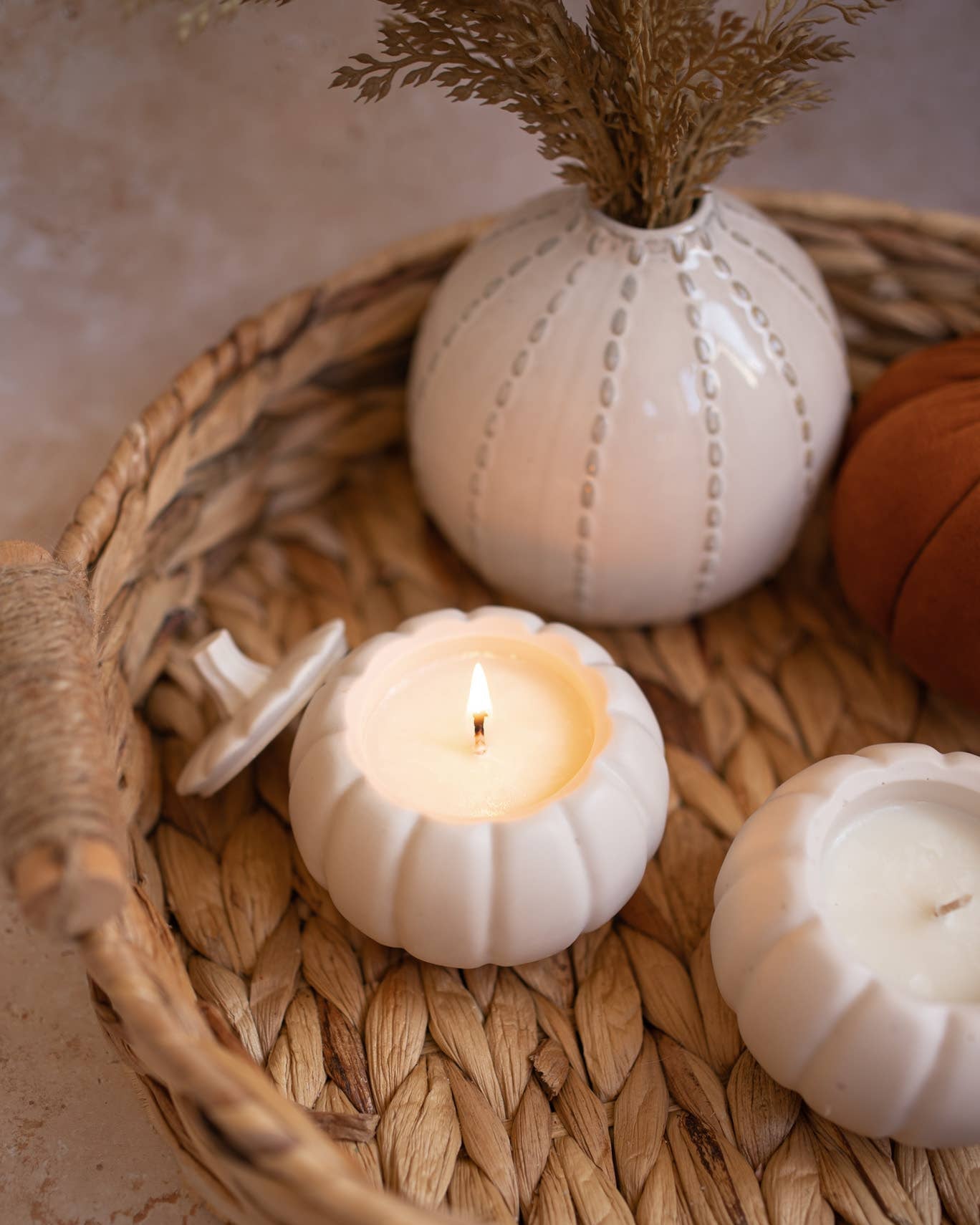 White ceramic vases with a lit candle inside on a woven basket