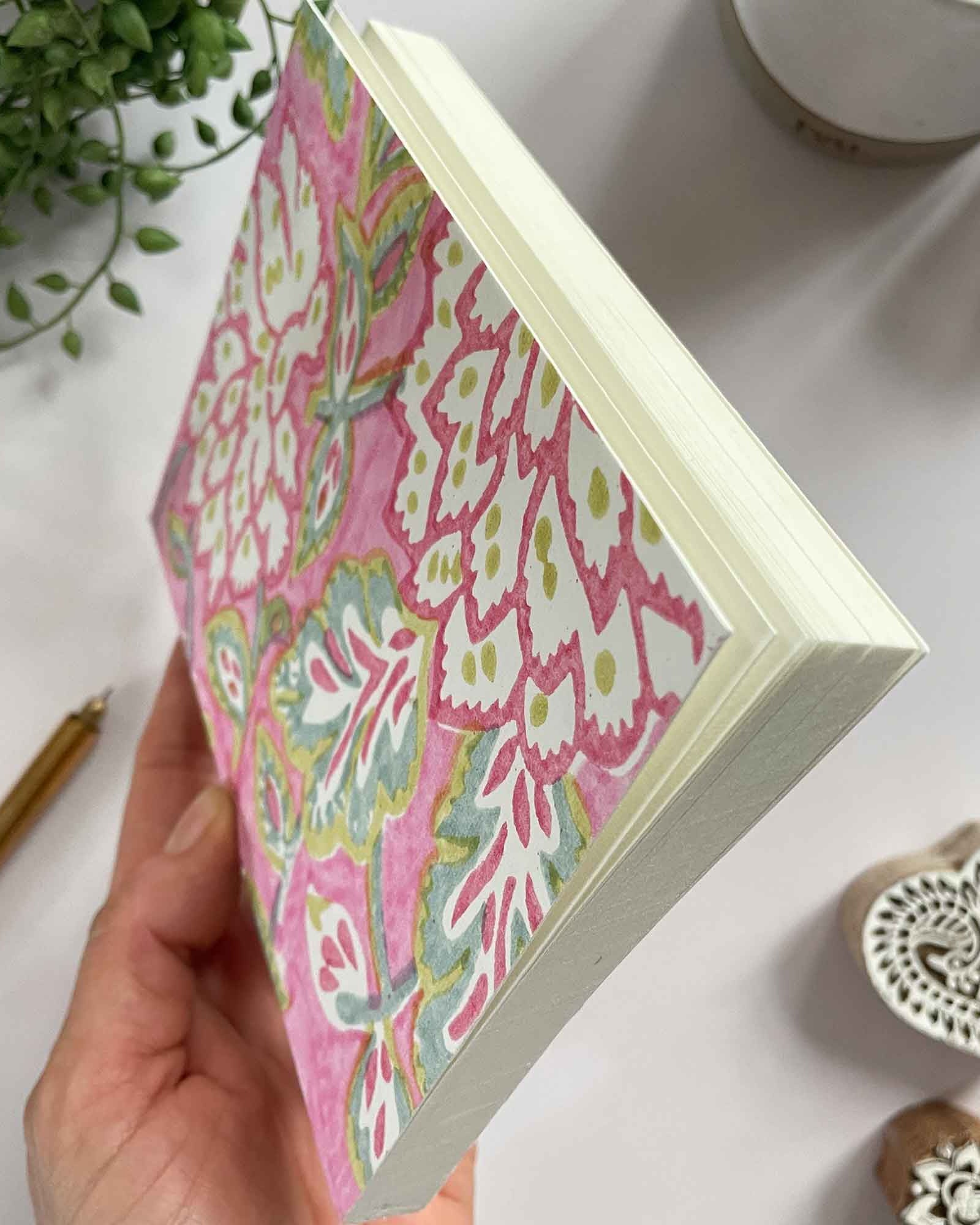 Hand holding a box with pink floral pattern on a white surface with decorative items.