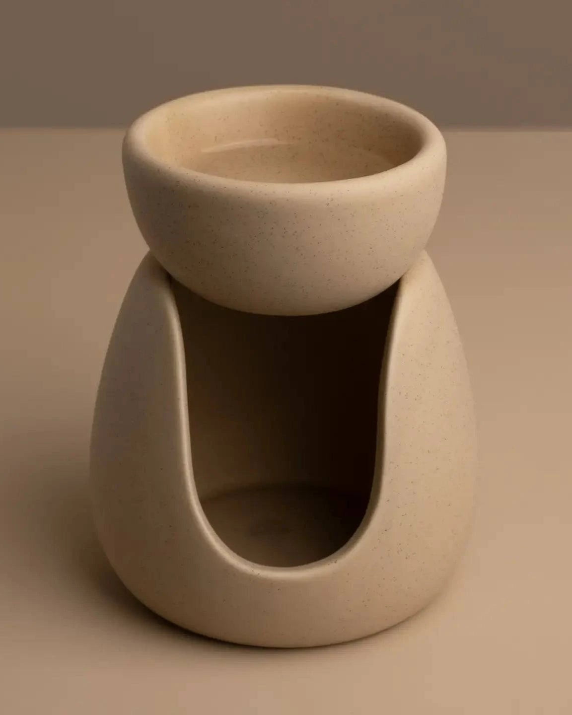 Beige ceramic wax melt burner on a neutral table and background