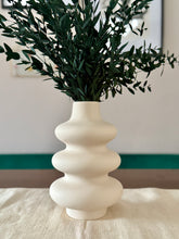 White ceramic vase with green foliage on a light surface