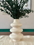 White ceramic vase with green foliage on a light surface