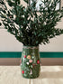 Decorative vase with floral patterns containing green plants on a neutral background