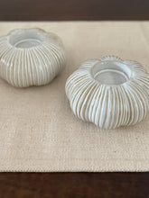 Two ribbed ceramic candle holders on a textured surface
