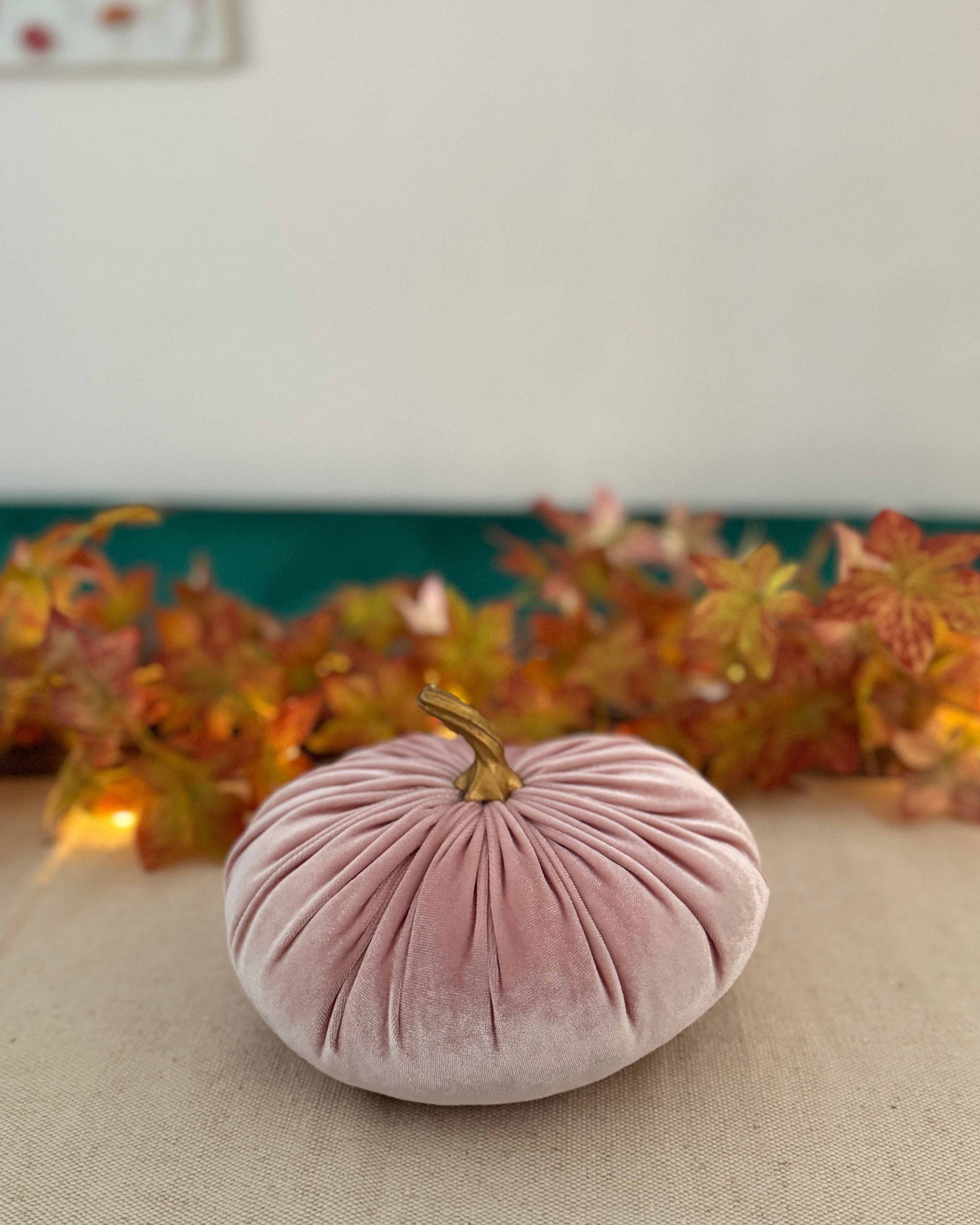 Pink velvet pumpkin on a table with autumn leaves in the background