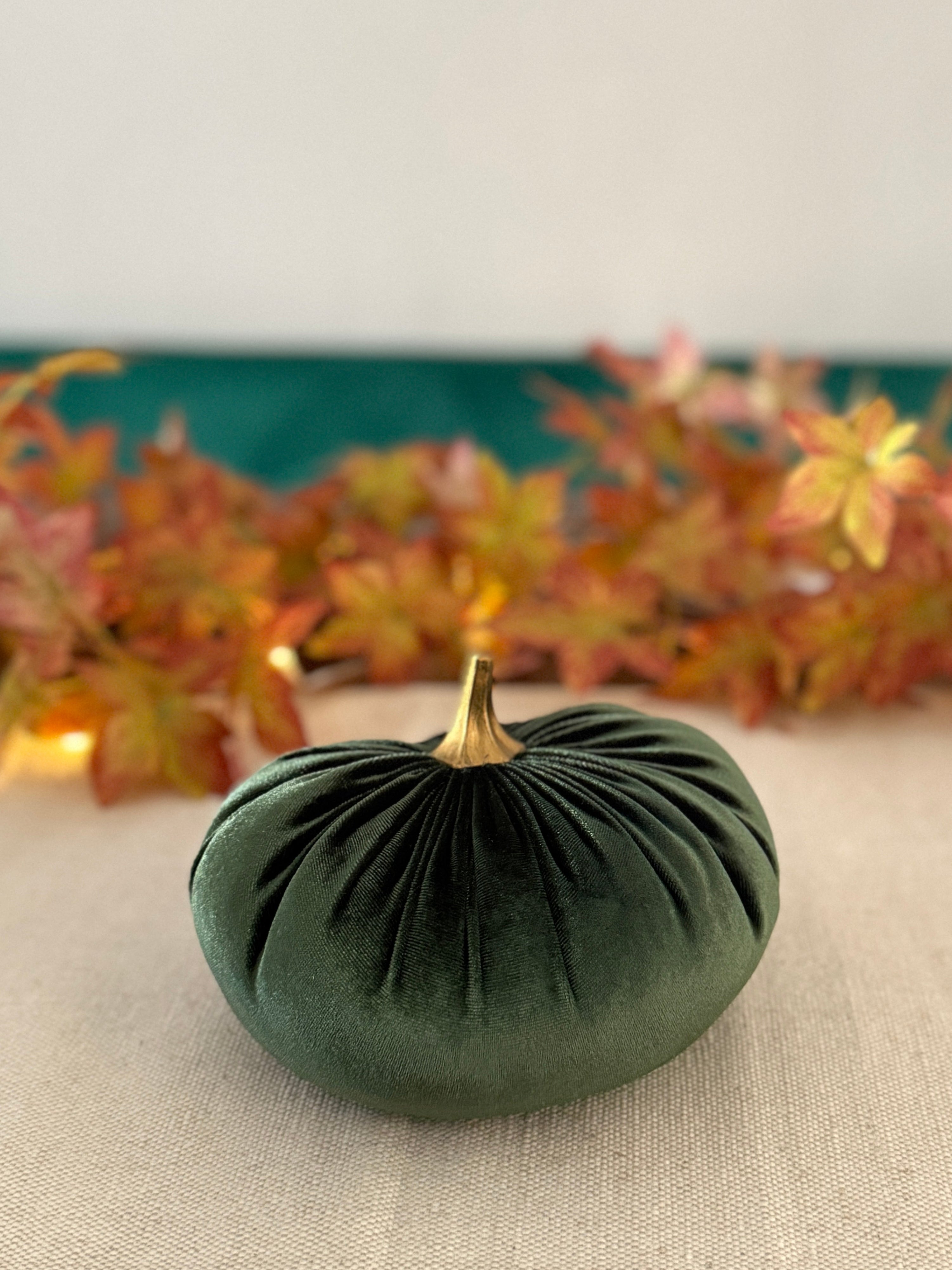 Green decorative pumpkin on a table with autumn leaves in the background