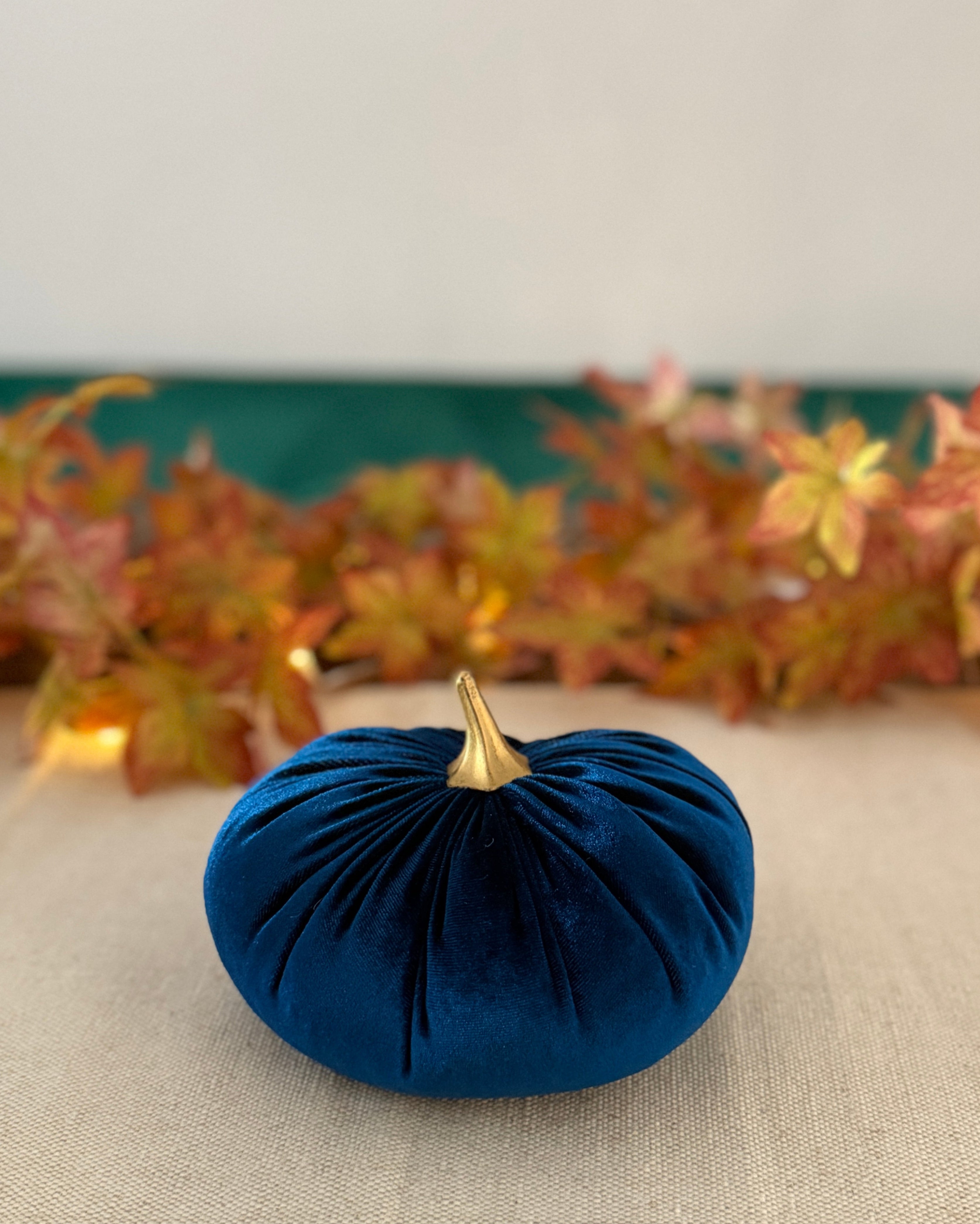Blue velvet pumpkin with a gold stem on a tablecloth with autumn leaves in the background