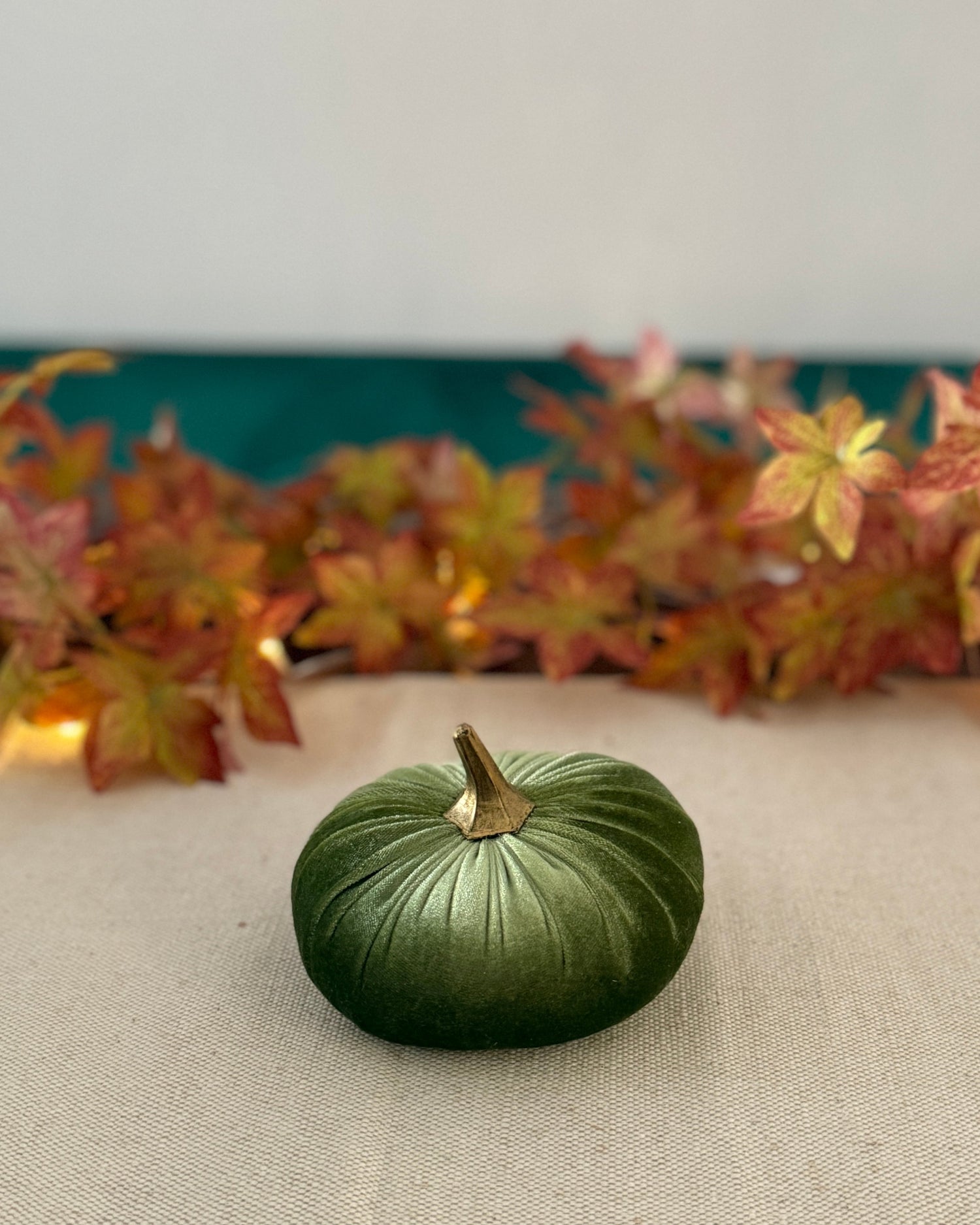 Small green pumpkin on a beige surface with autumn leaves in the background