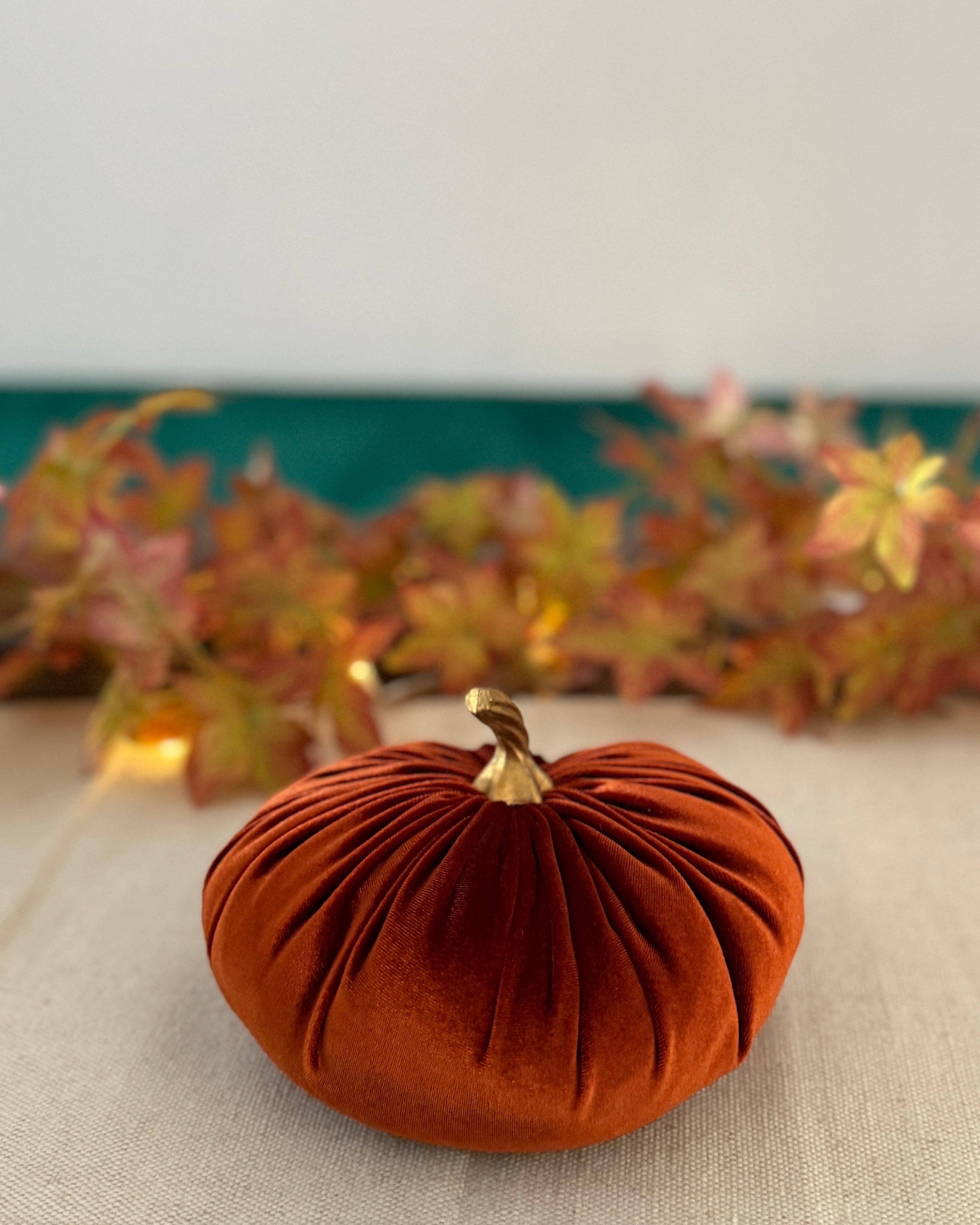 Small orange velvet pumpkin on a table with a decorative leaf garland in the background.
