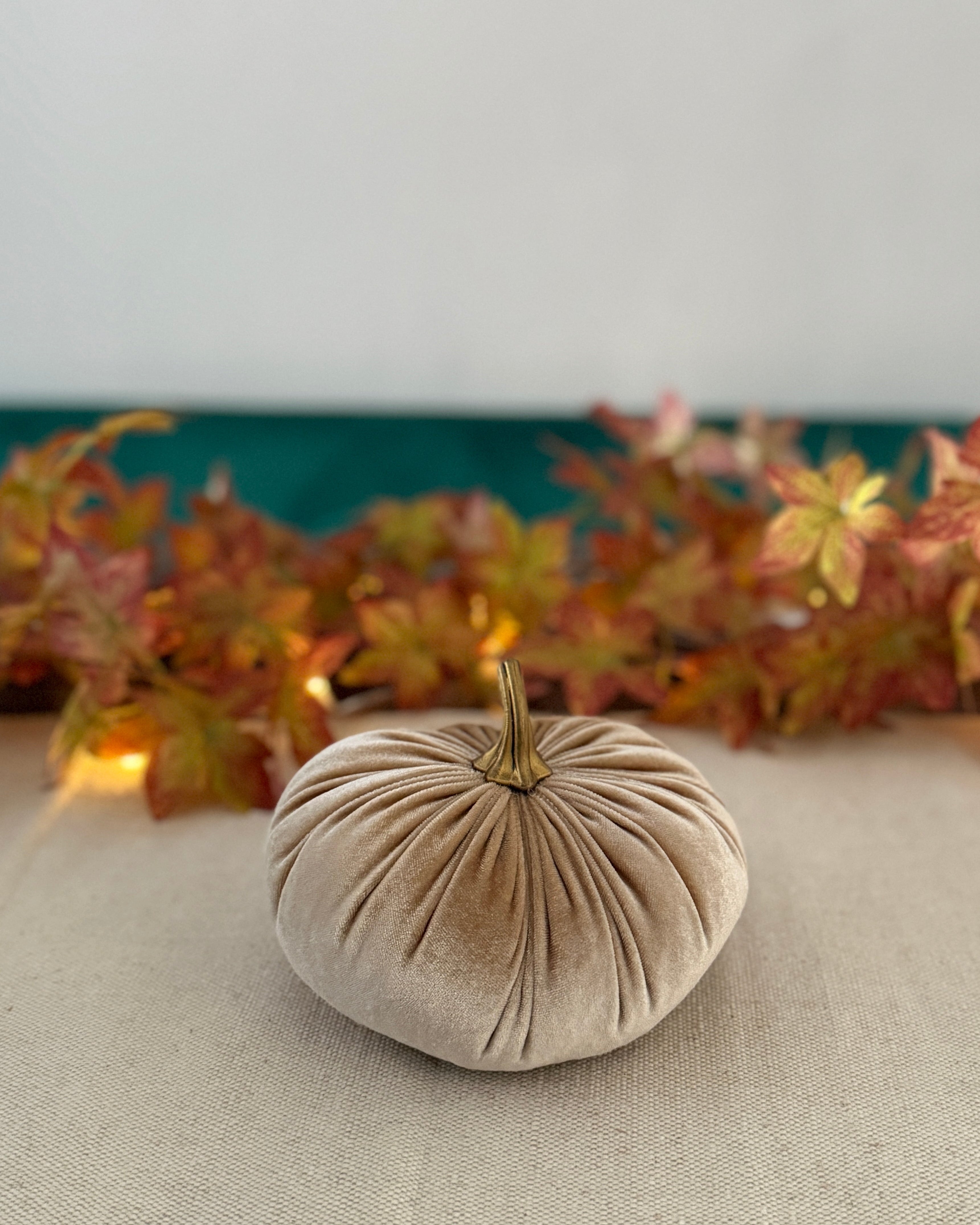Beige fabric pumpkin on a table with autumn leaves in the background