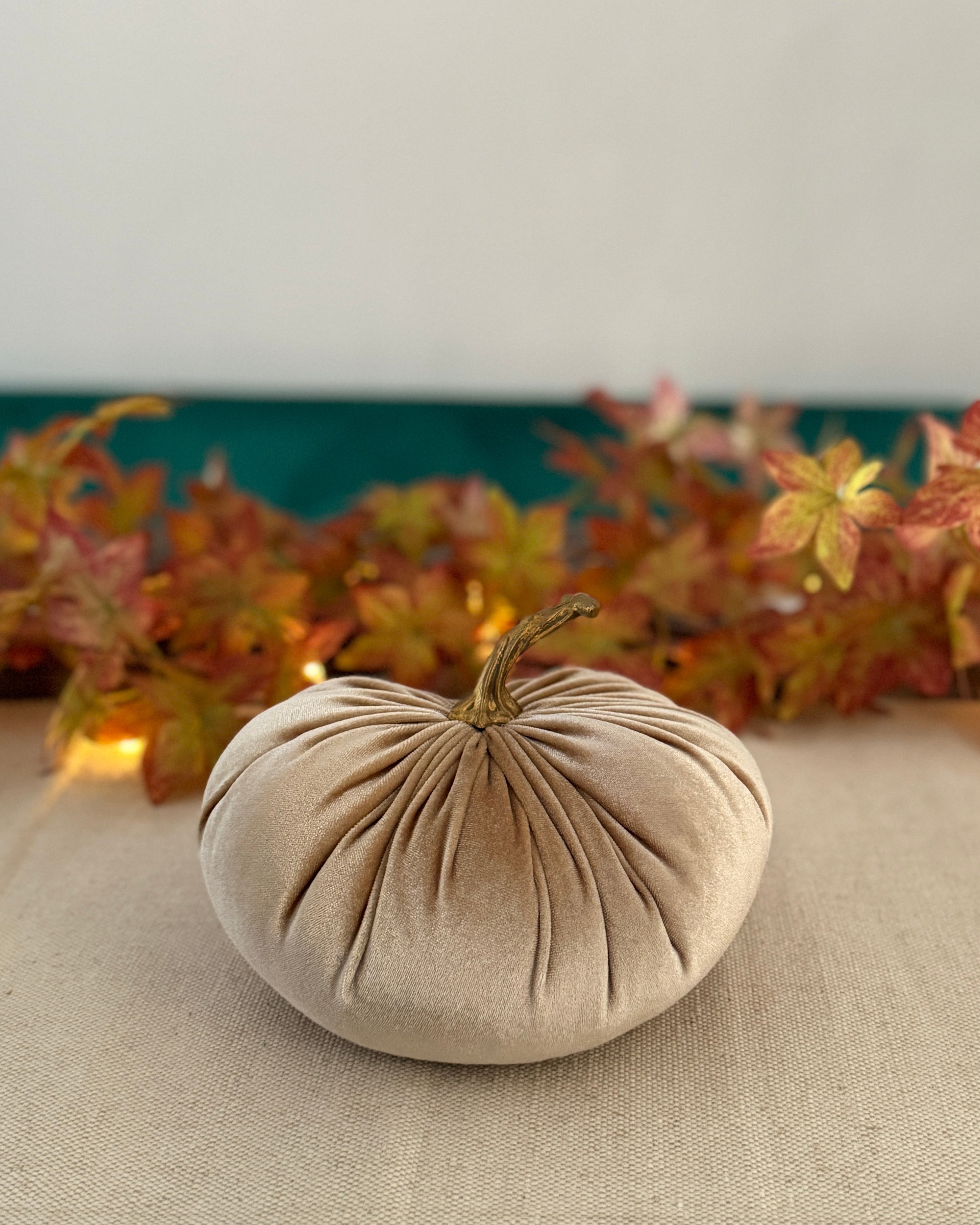 Beige fabric pumpkin on a table with autumn leaves in the background