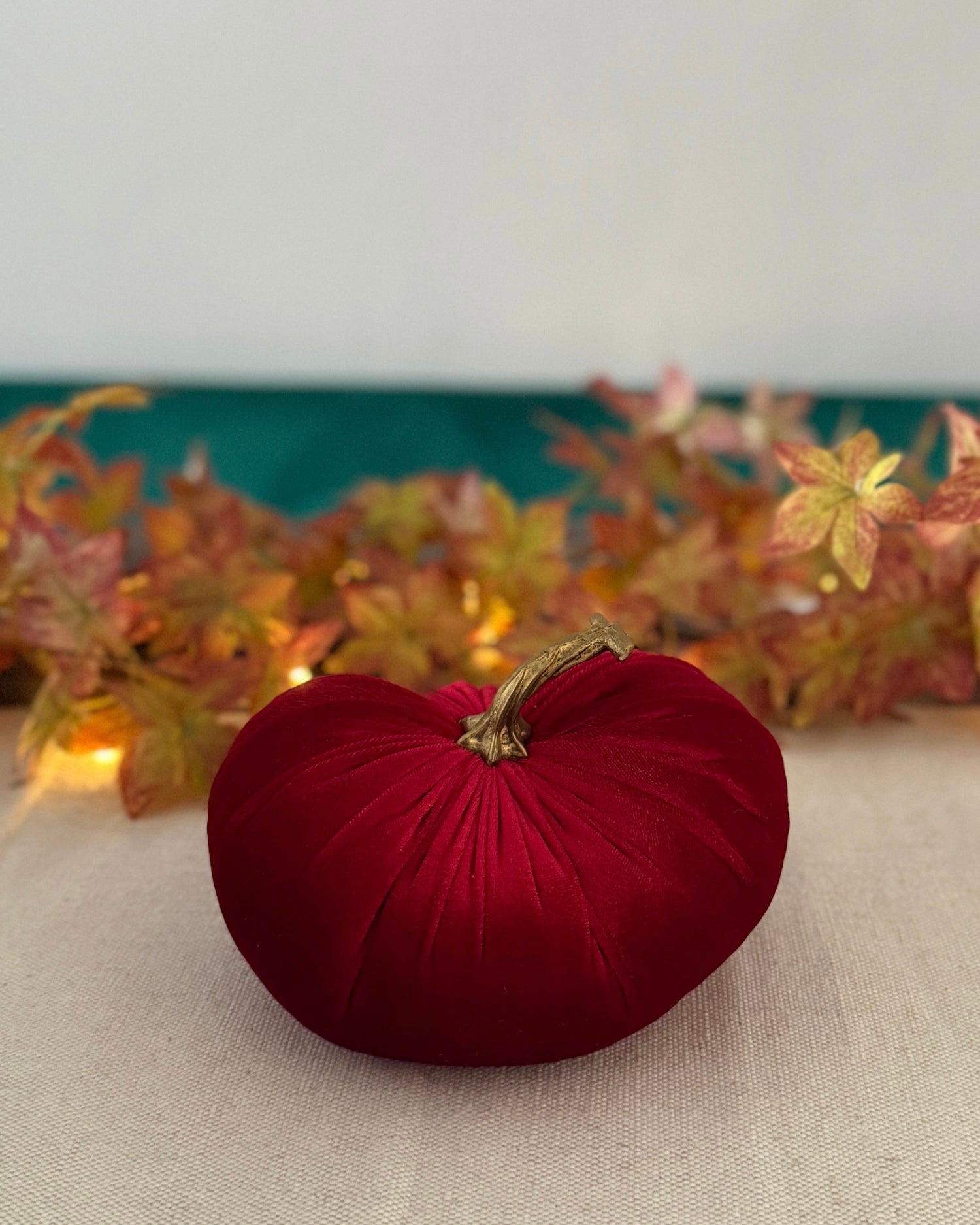Red decorative pumpkin on a neutral surface with autumn leaves in the background