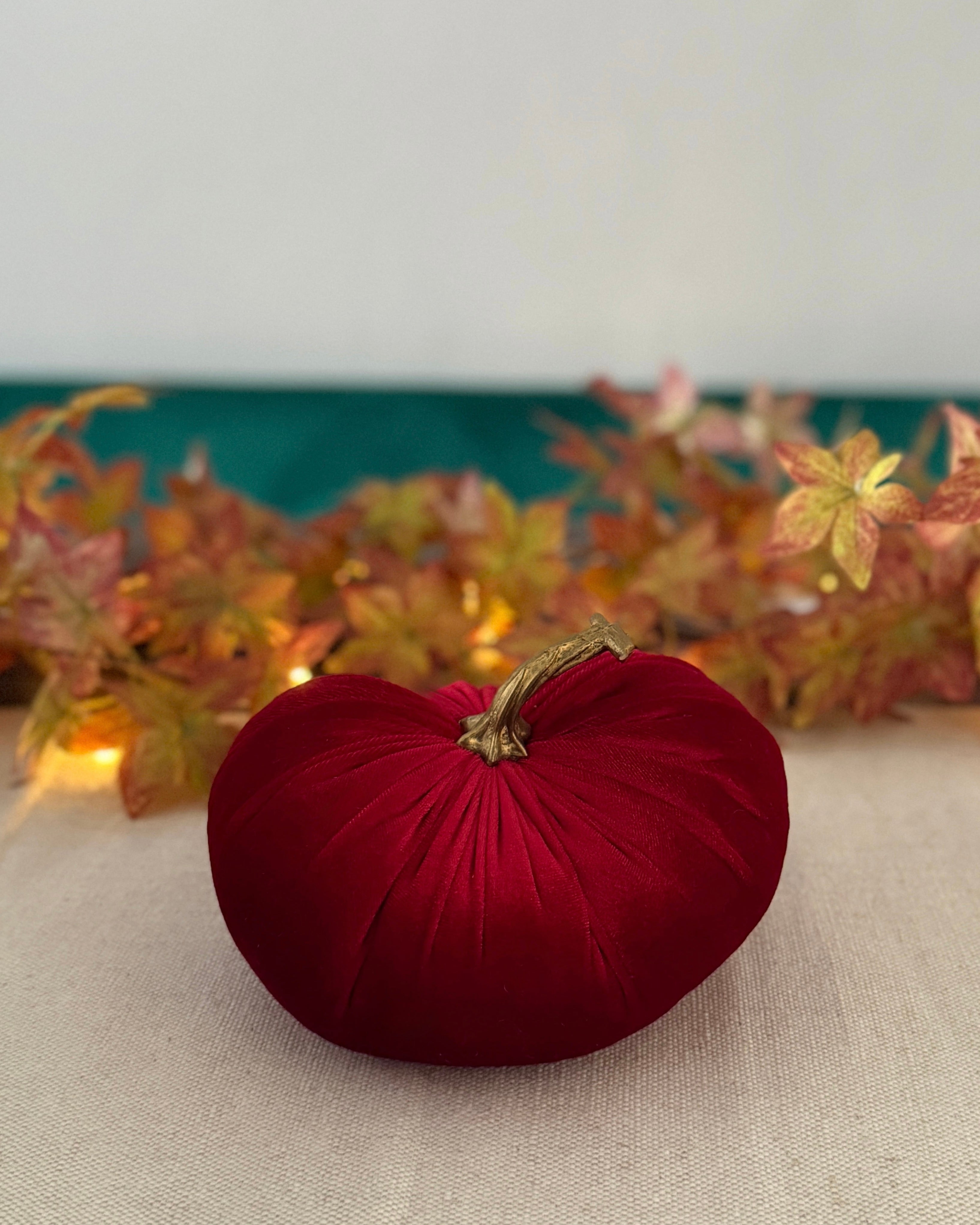 Red decorative pumpkin on a neutral surface with autumn leaves in the background