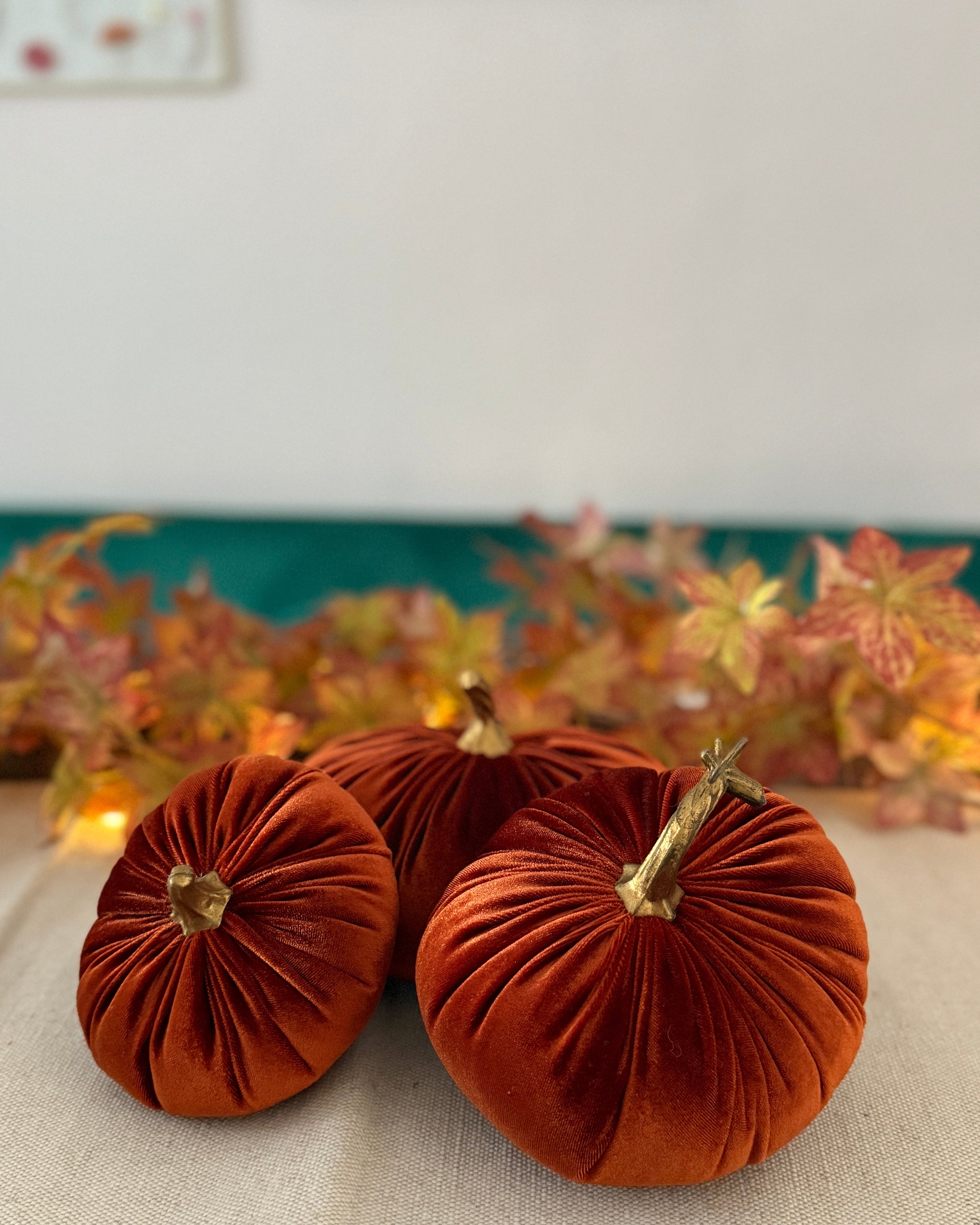 Three orange velvet pumpkins on a table with a decorative background