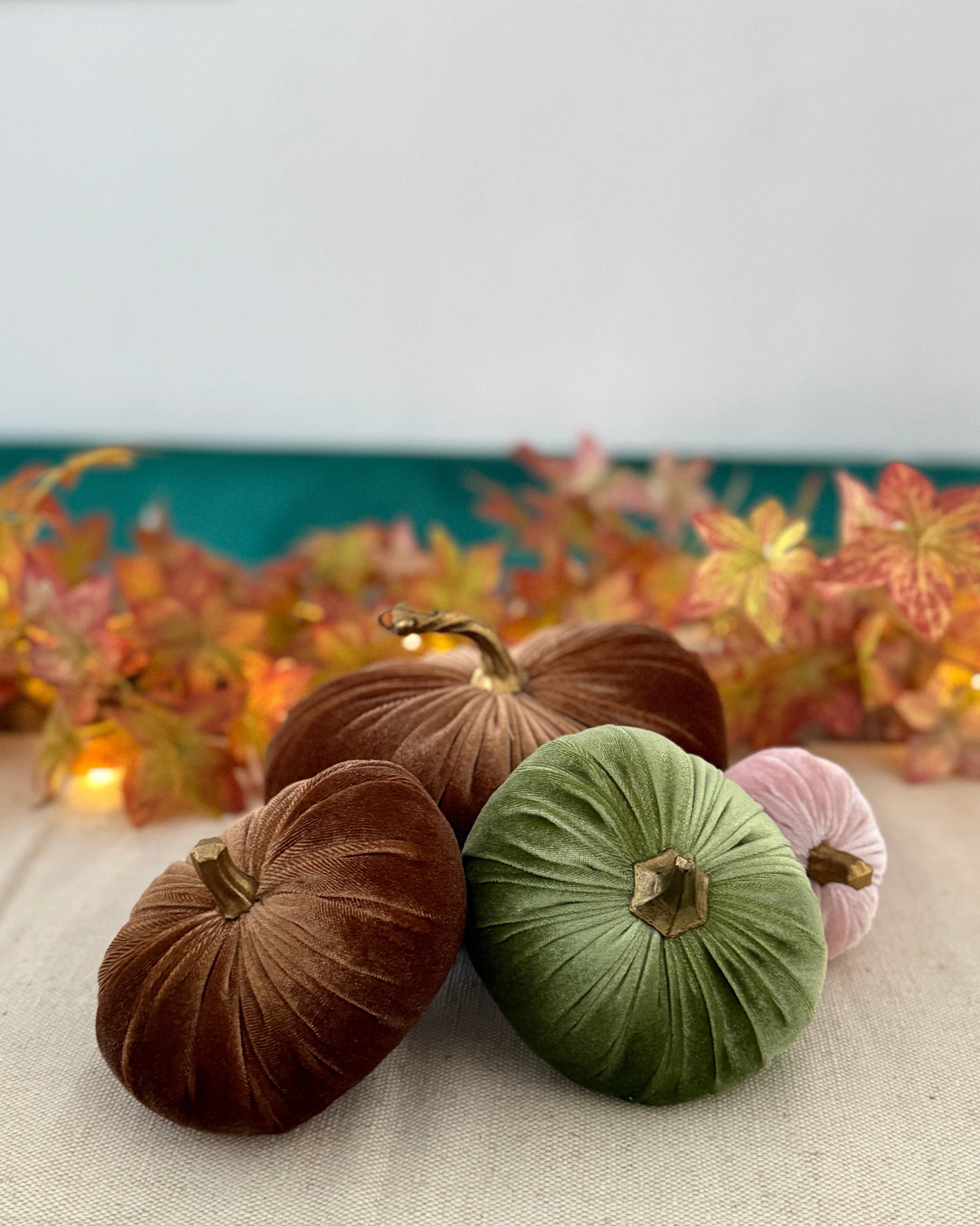 Decorative pumpkins in brown, green, and pink on a table with a festive background.