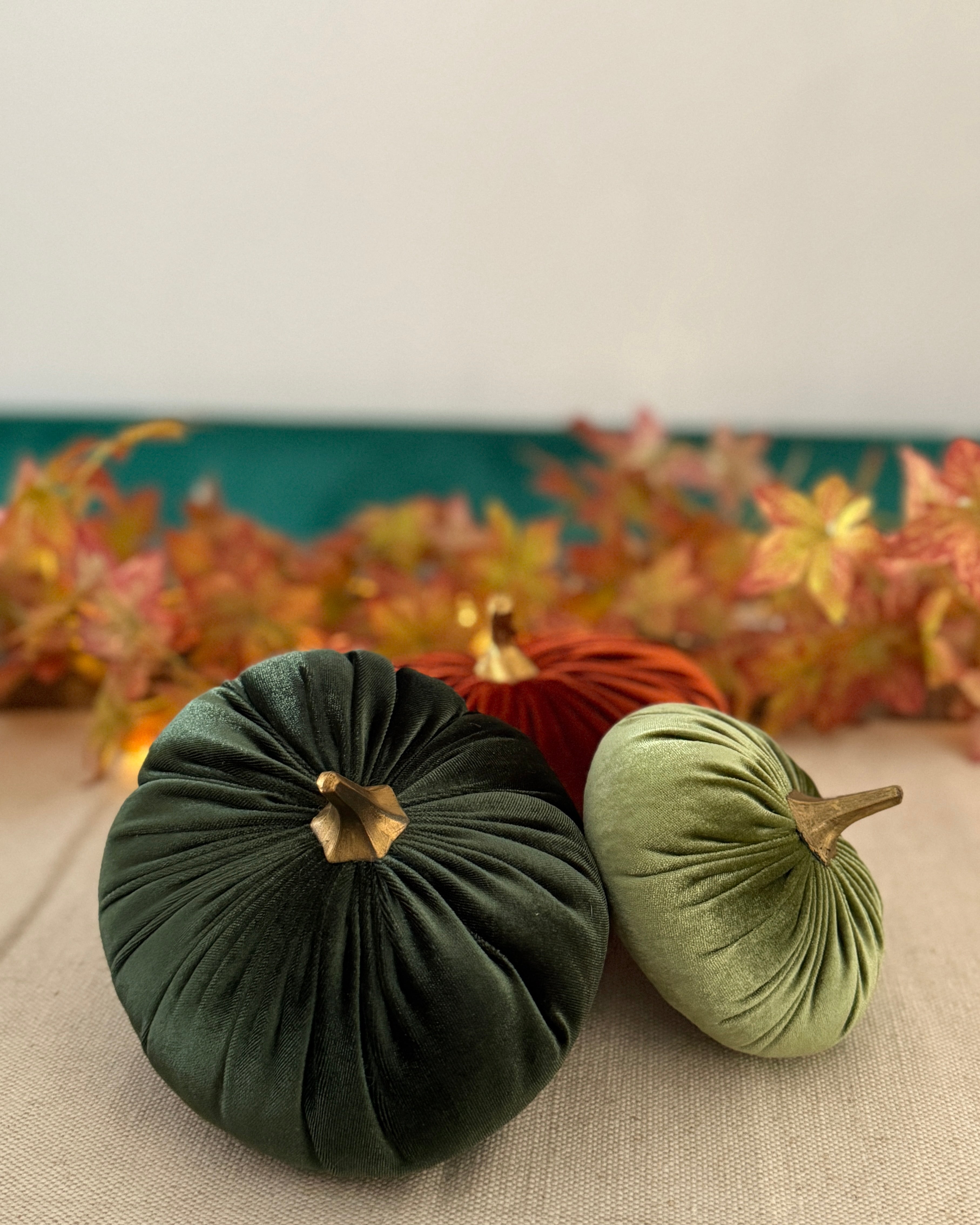 Three decorative pumpkins on a table with a blurred autumn-themed background