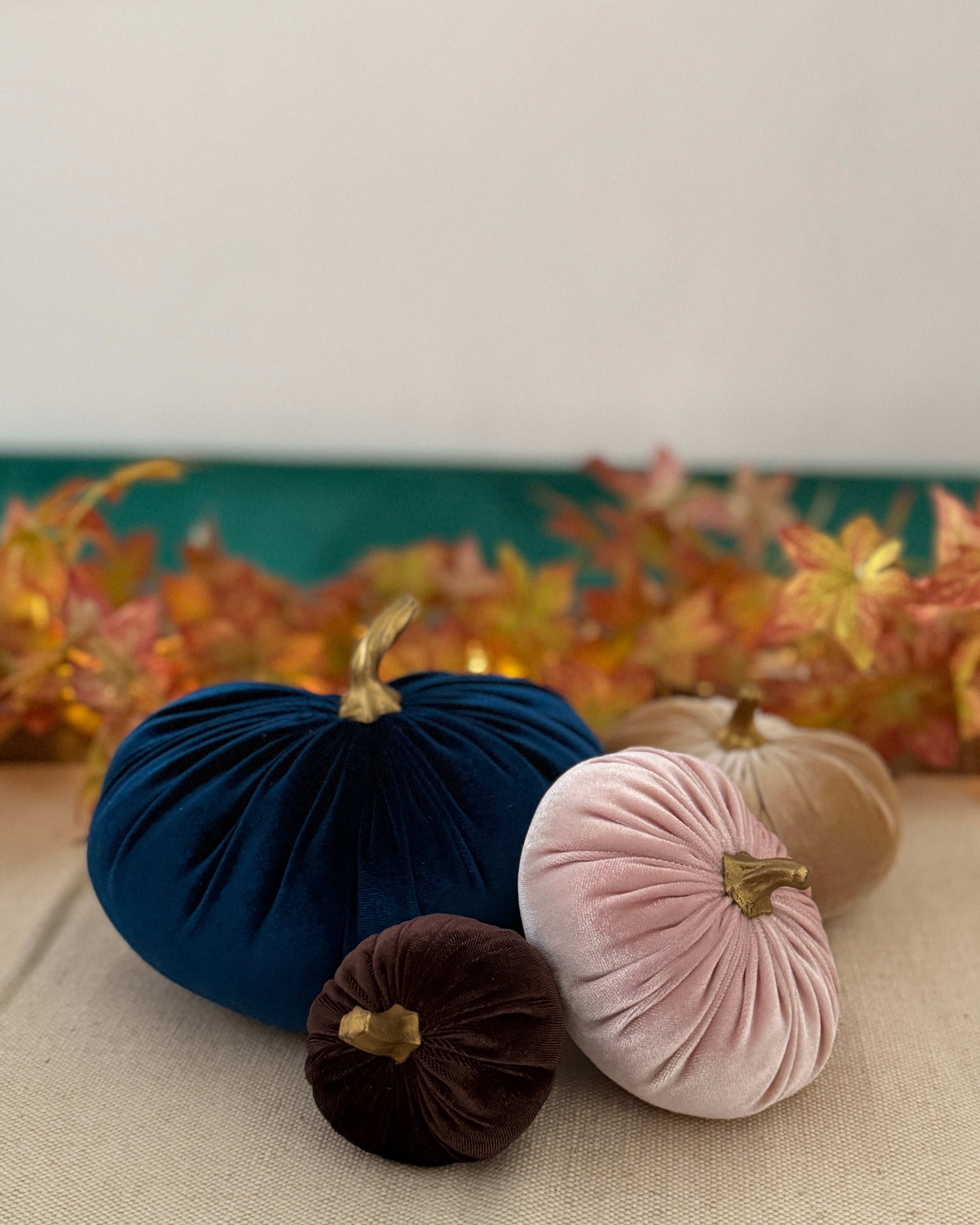 Decorative pumpkins in navy, pink, and brown on a table with a floral arrangement in the background.