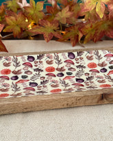Decorative fabric with floral pattern in a wooden frame, next to a plant.