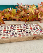 Wooden tray with floral patterned mat on a neutral background with autumn leaves.