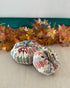 Two patchwork-style fabric pumpkins on a neutral surface with autumn leaves in the background.