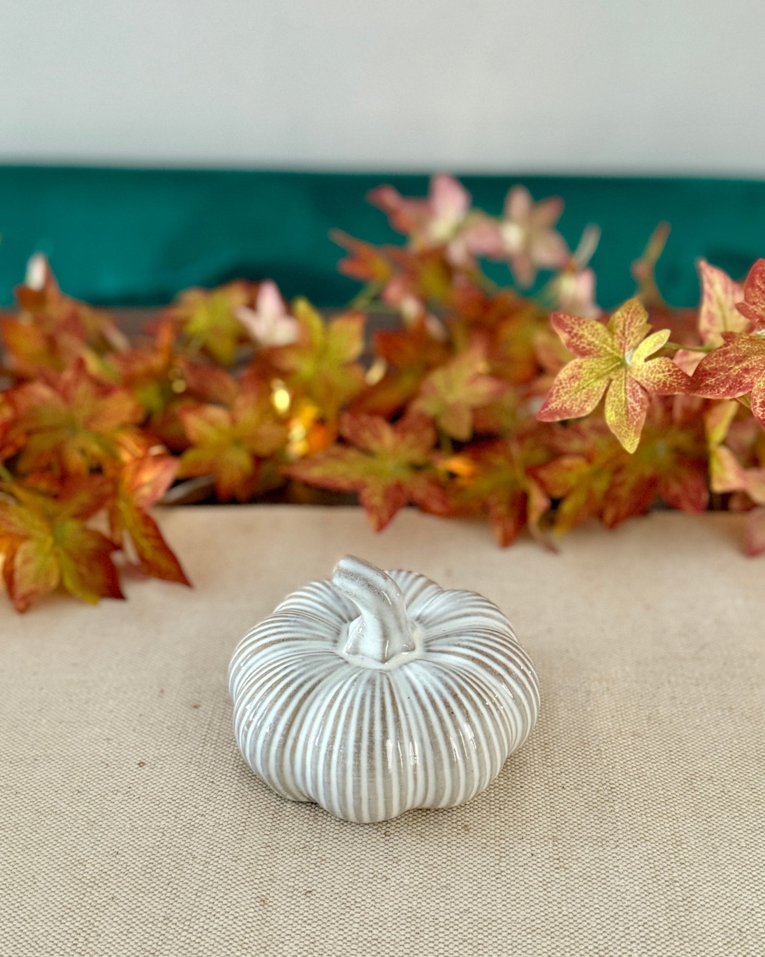 Decorative white pumpkin on a textured surface with autumn leaves in the background