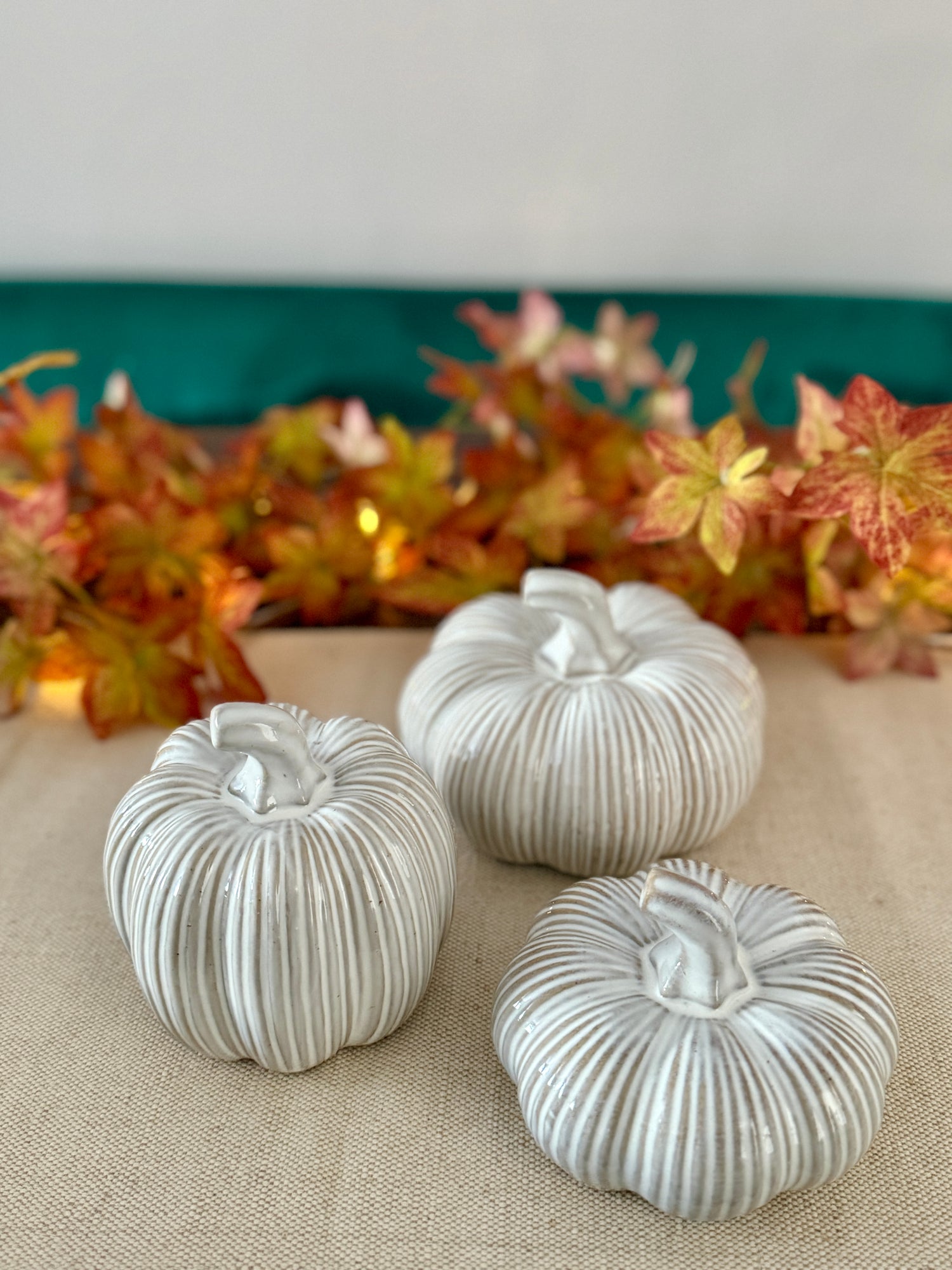 Three ribbed ceramic pumpkins on a textured surface with a decorative leaf background.