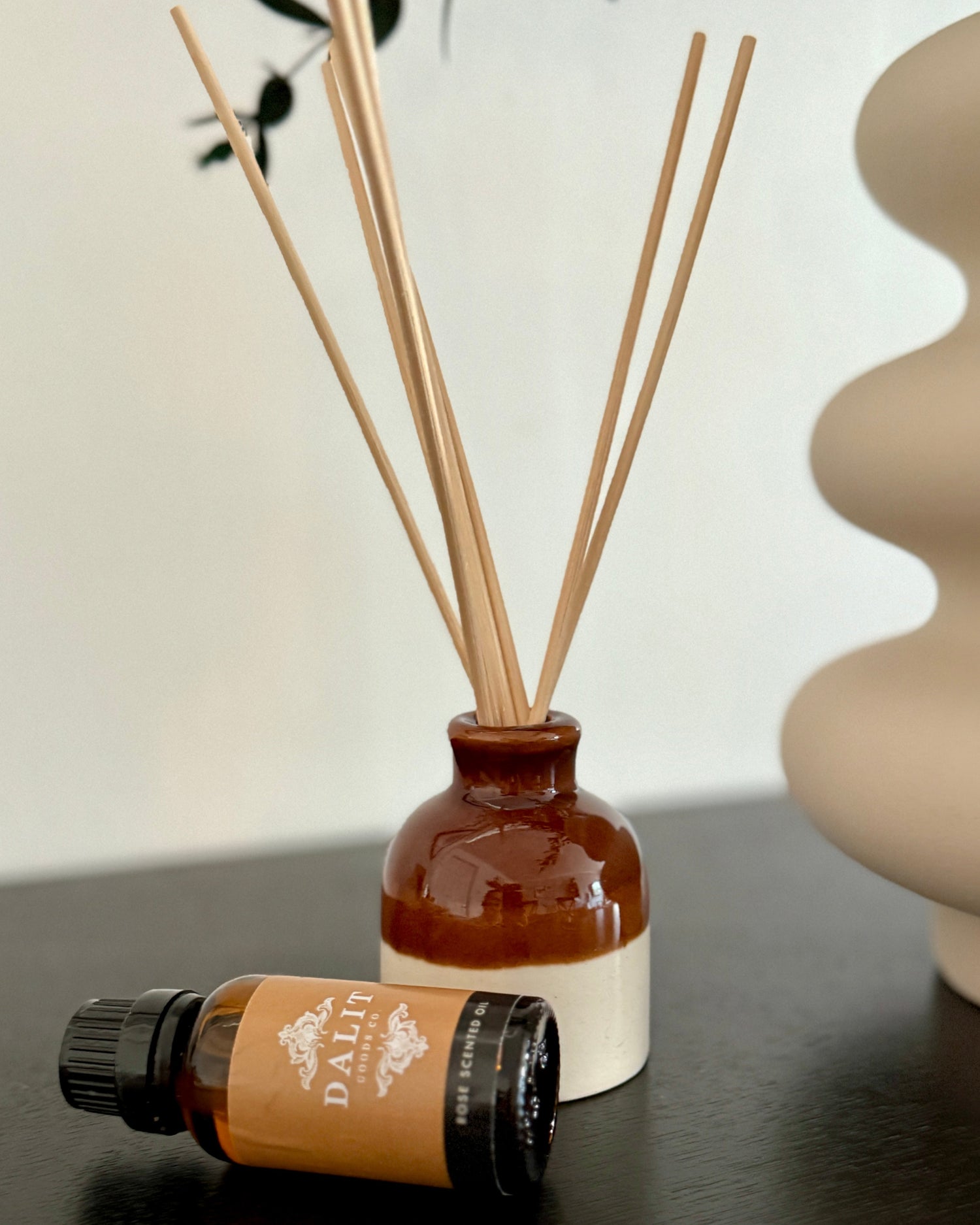 Diffuser bottle with reeds and a small bottle of essential oil on a dark surface.