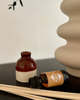 Brown bottle, white vase, and reed diffuser on a dark surface with a neutral background