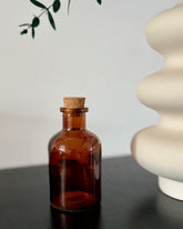 Brown glass bottle with cork on a dark surface with a light gray background