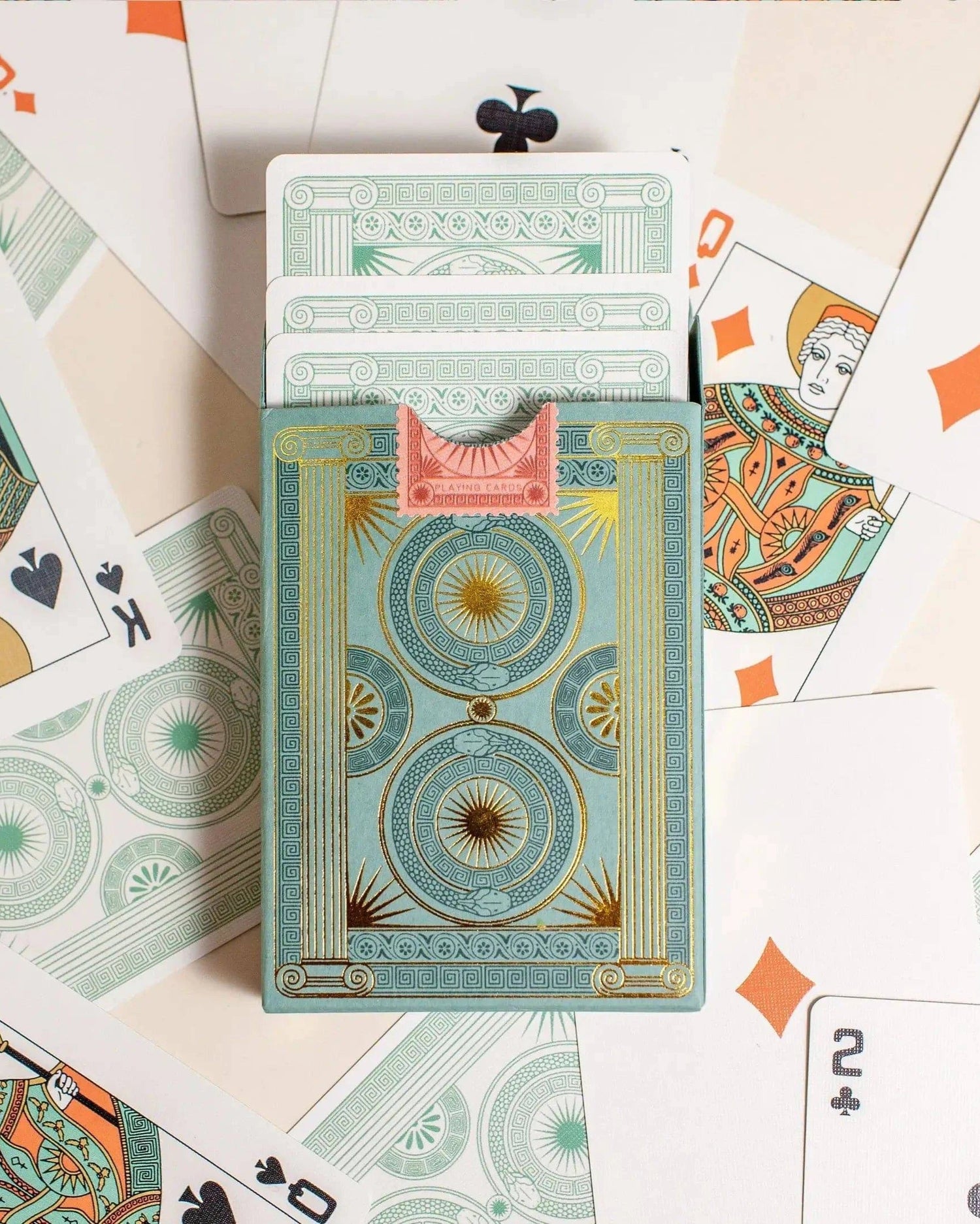 Premium-grade playing cards in sage green with a gold-foiled tuck box featuring an ace of spades design with a snake wrapped around it. Back of box with cards coming out surrounded by cards