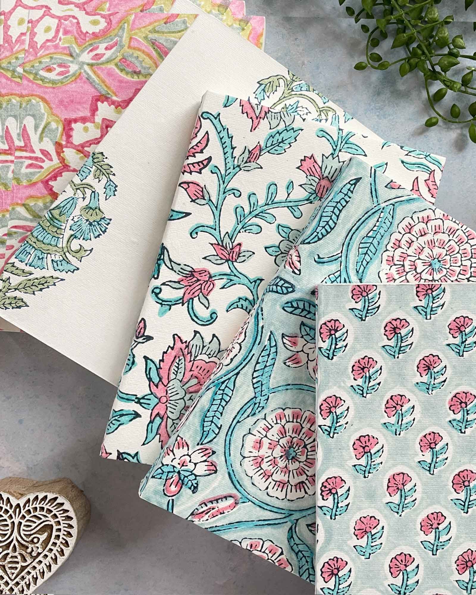 Floral patterned fabric swatches on a gray surface with a plant and wooden block in the background.