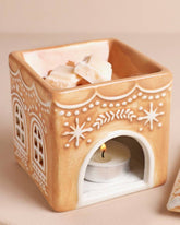 Decorative ceramic wax warmer with a lit candle on a beige background