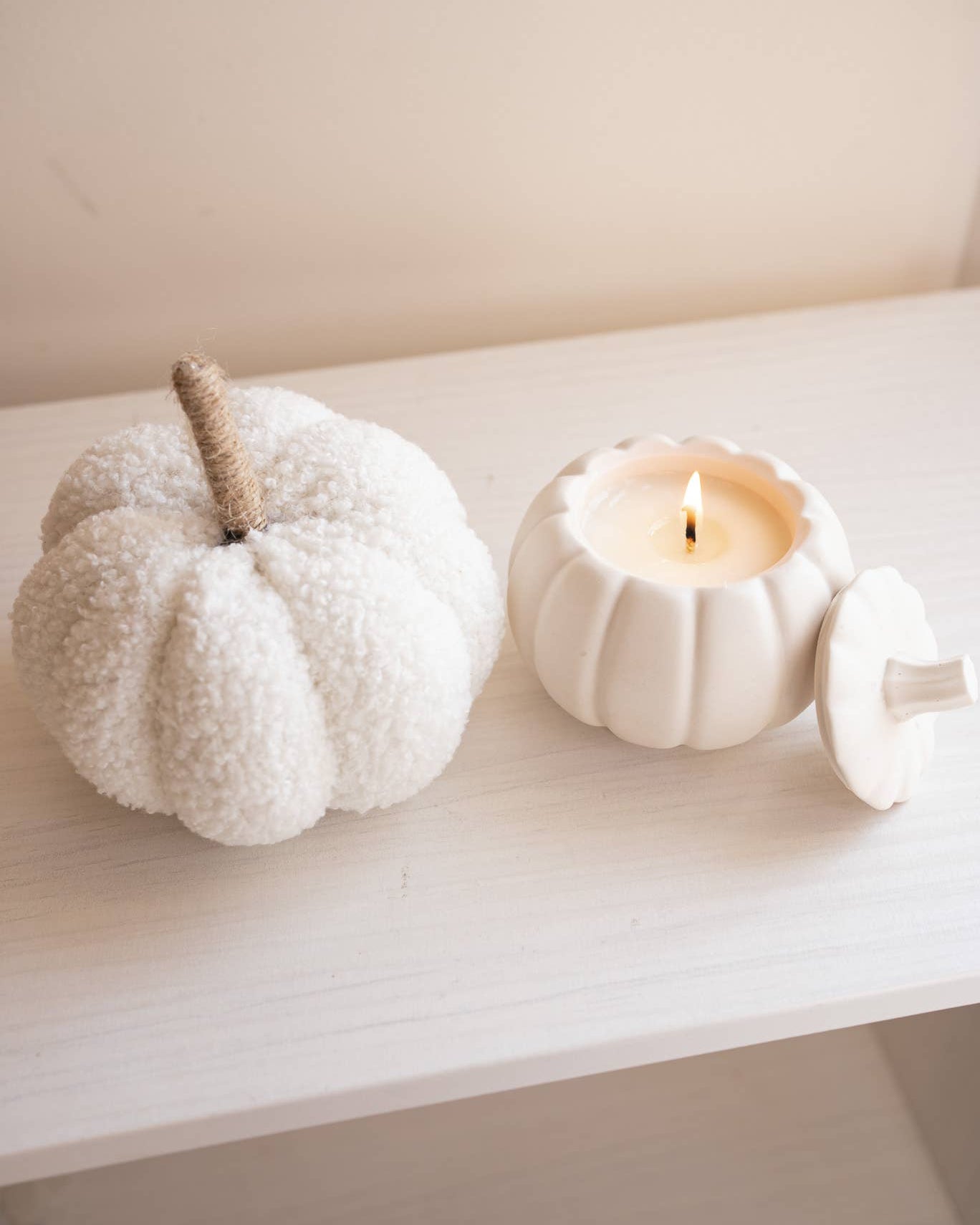 Two white pumpkins with a candle on a light surface