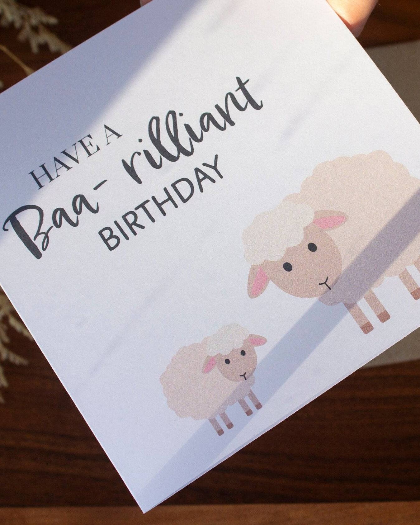 Square handmade birthday card with a sheep and lamb illustration and "Have a Baa-rilliant Birthday" text. Made in the UK using sustainable card stock and eco-friendly packaging.