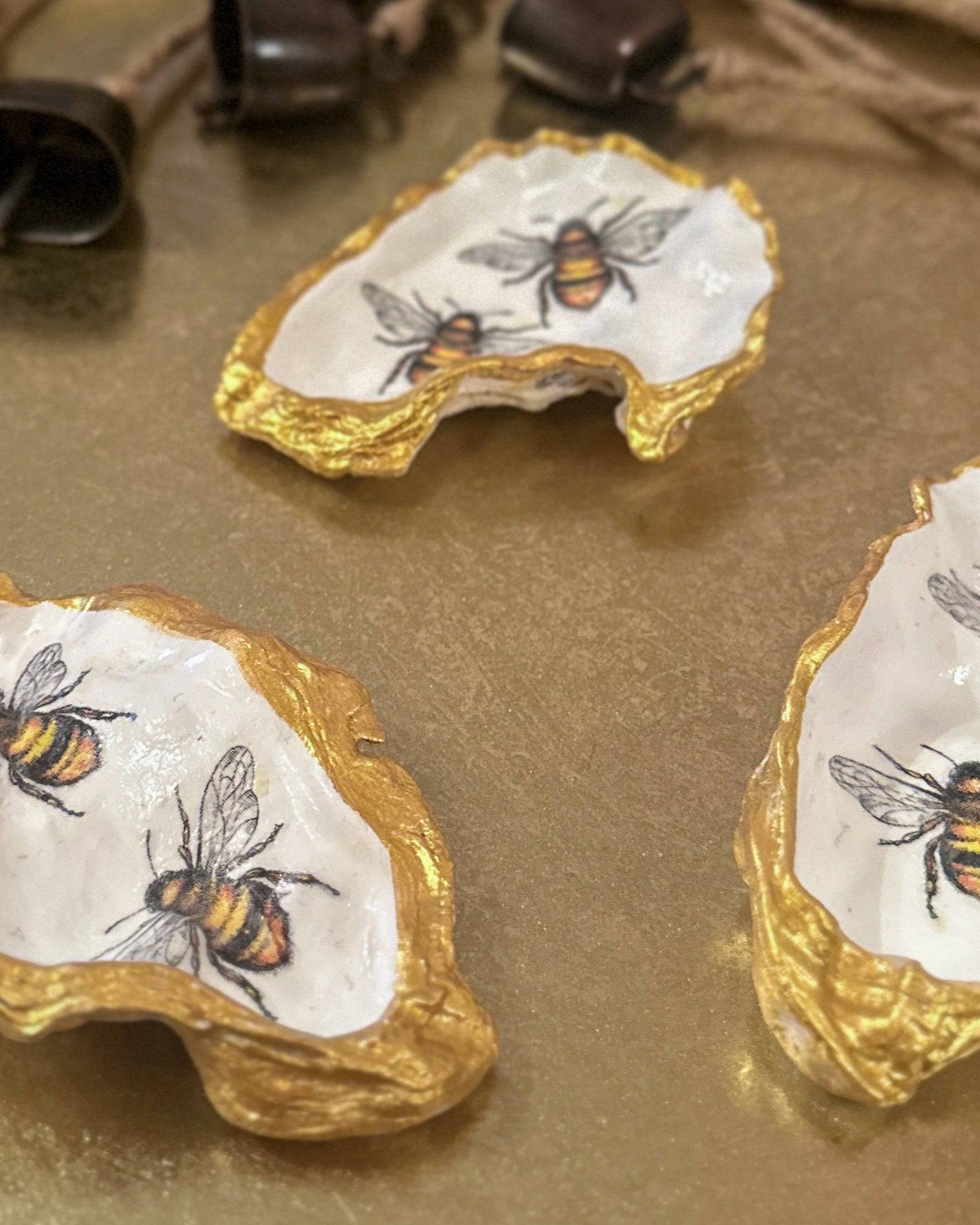 Handmade oyster shells trinket trays featuring two bumble bees, crafted using a meticulous decoupage technique with hand-painted gold edges, perfect for spring jewellery storage or home decor.