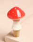 Mushroom-shaped bottle stopper with red cap and white body on a beige background