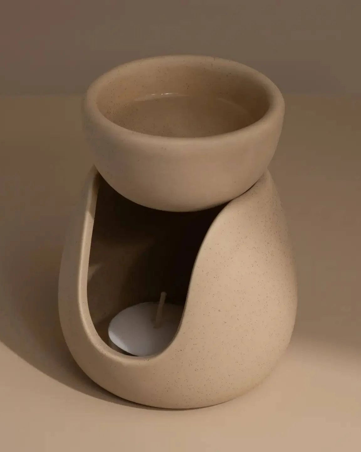 Beige ceramic wax melt burner with tea light on a neutral table and background