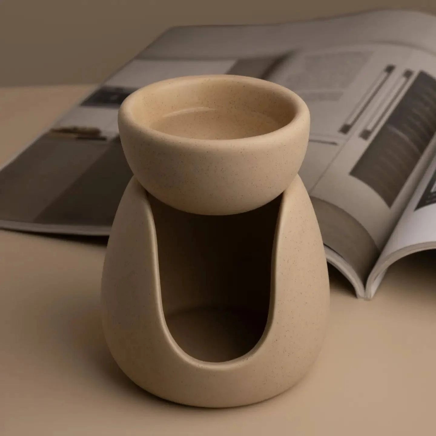 Beige ceramic wax melt burner on a neutral table and magazine open in background