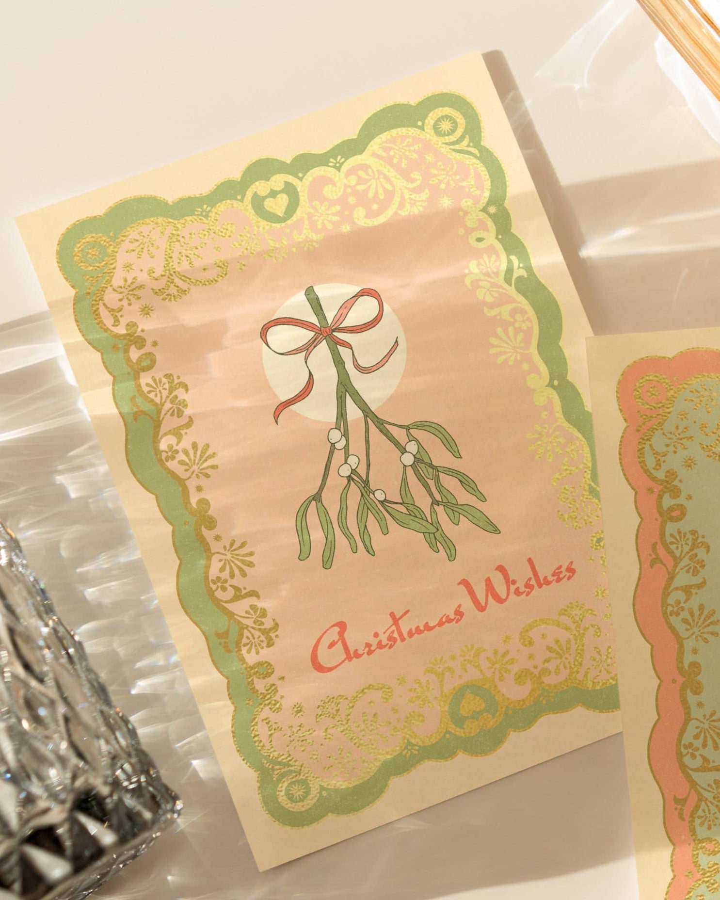 A6 handmade eco-conscious card with a soft pink background, green mistletoe accents, and luxe gold foil. Includes a Kraft envelope and biodegradable cello wrap.