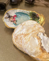 Handmade oyster shell trinket dish featuring an Easter bunny and open egg shell illustration, crafted with a decoupage technique and hand-painted gold edges, perfect for Easter or springtime gifts.