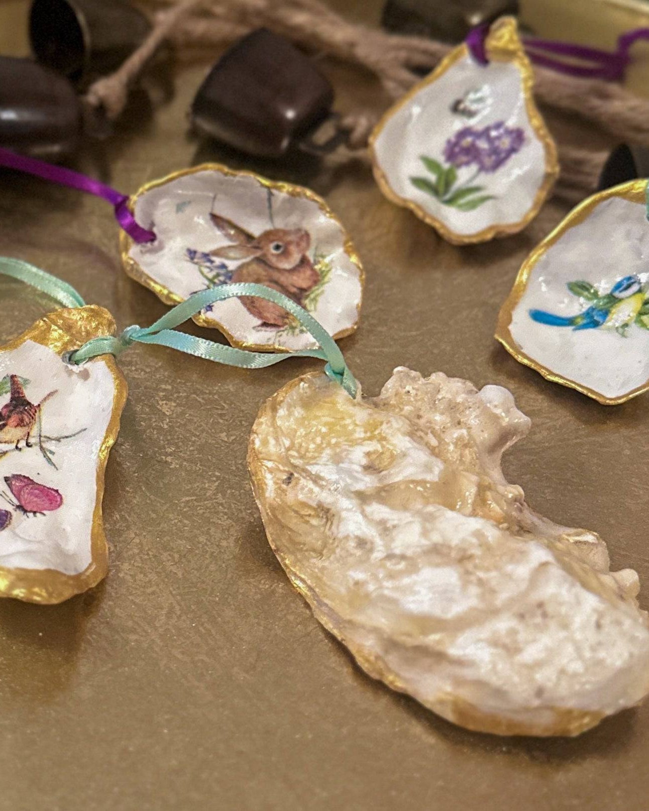 Set of five handmade Easter hanging ornaments crafted from oyster shells, featuring a decoupage technique with hand-painted gold edges, decorated with spring motifs like bunnies, flowers, and bees, perfect for Easter or spring decor.