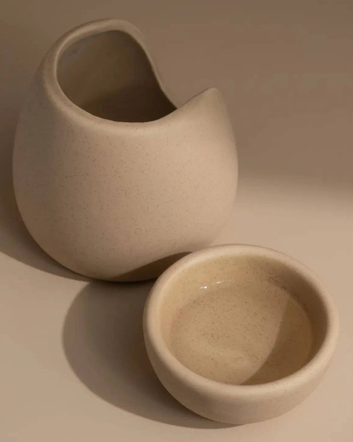 Beige ceramic wax melt burner top separate from burner on a neutral table and background